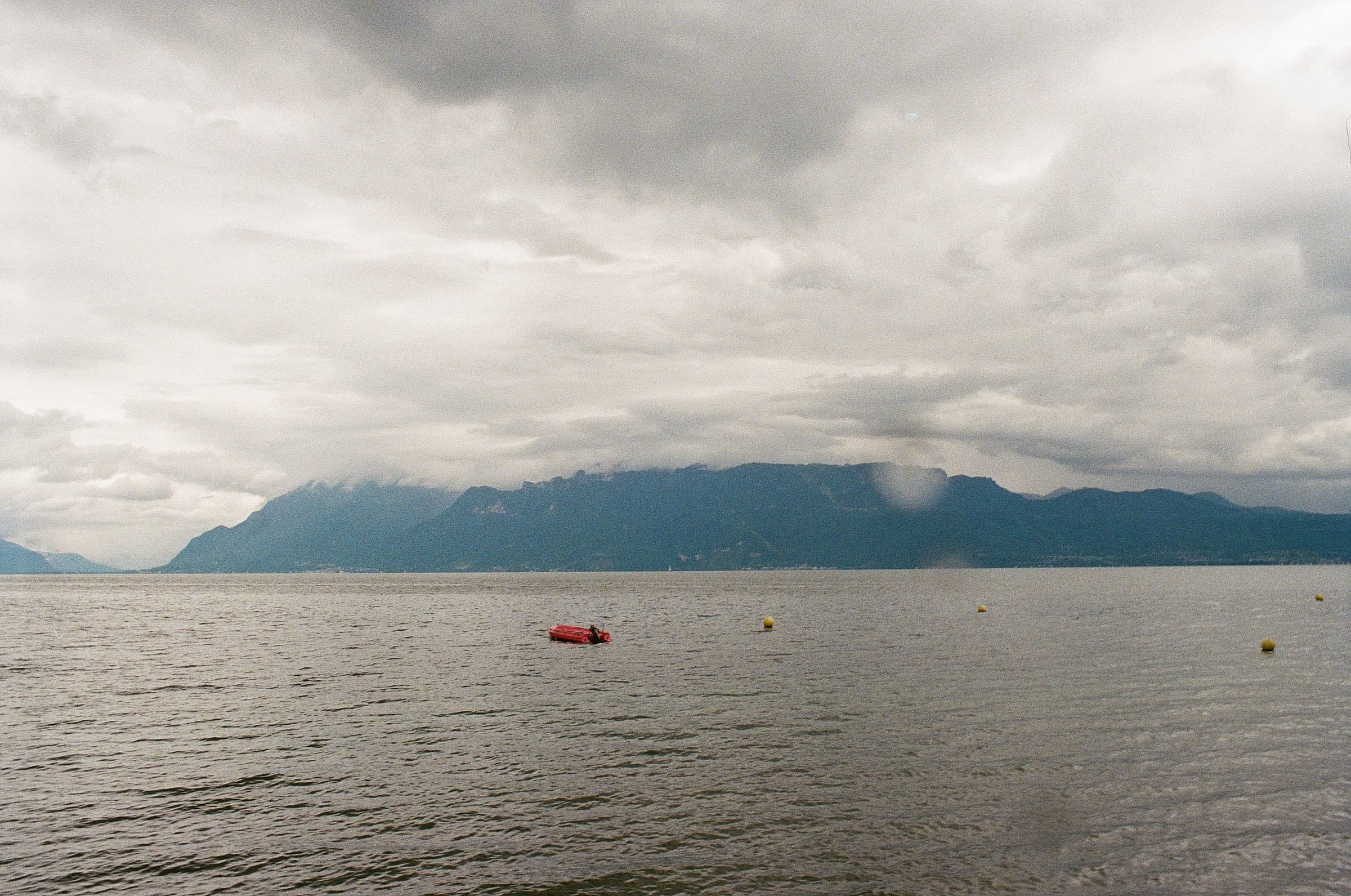 Landscape image of Lake Geneva with a single red boat and the Alps in the background