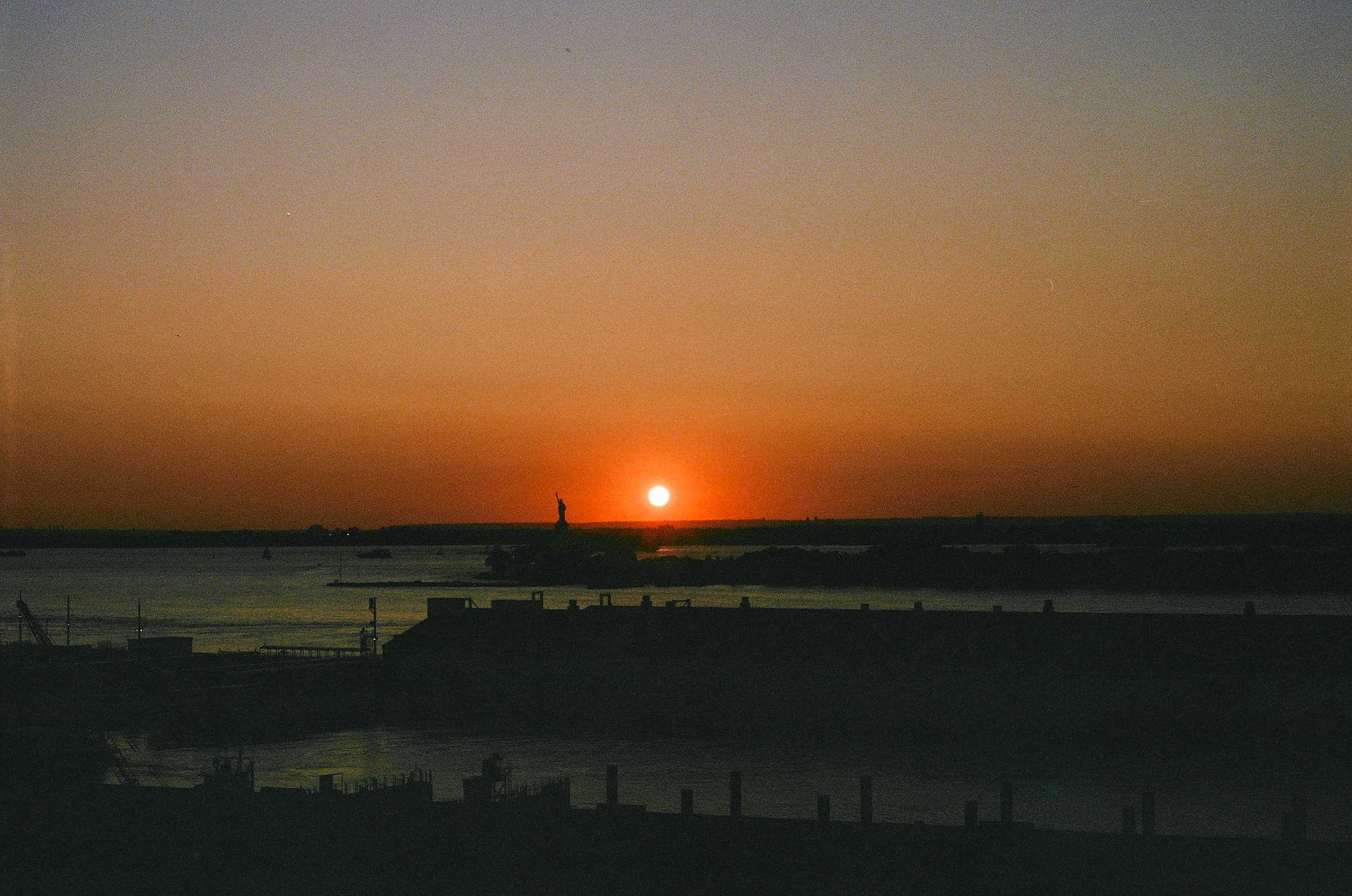 Landscape photo of the Red Hook area during sunset, with the Statue of Liberty in the background