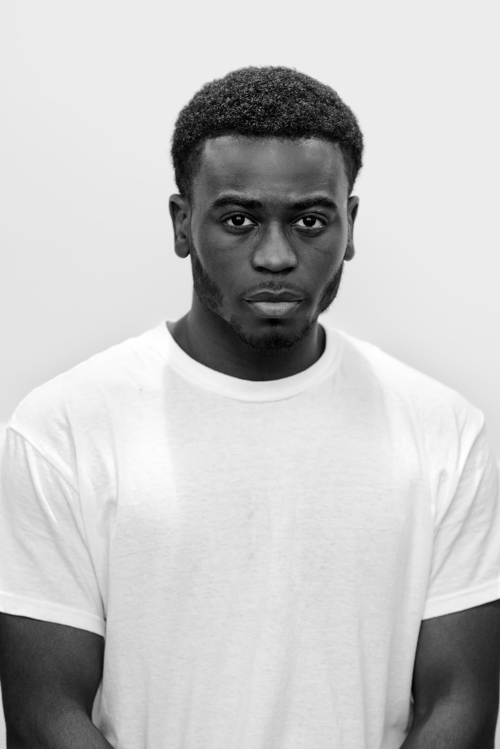 Black and white portrait of a man in a white tee, staring fiercely into the camera