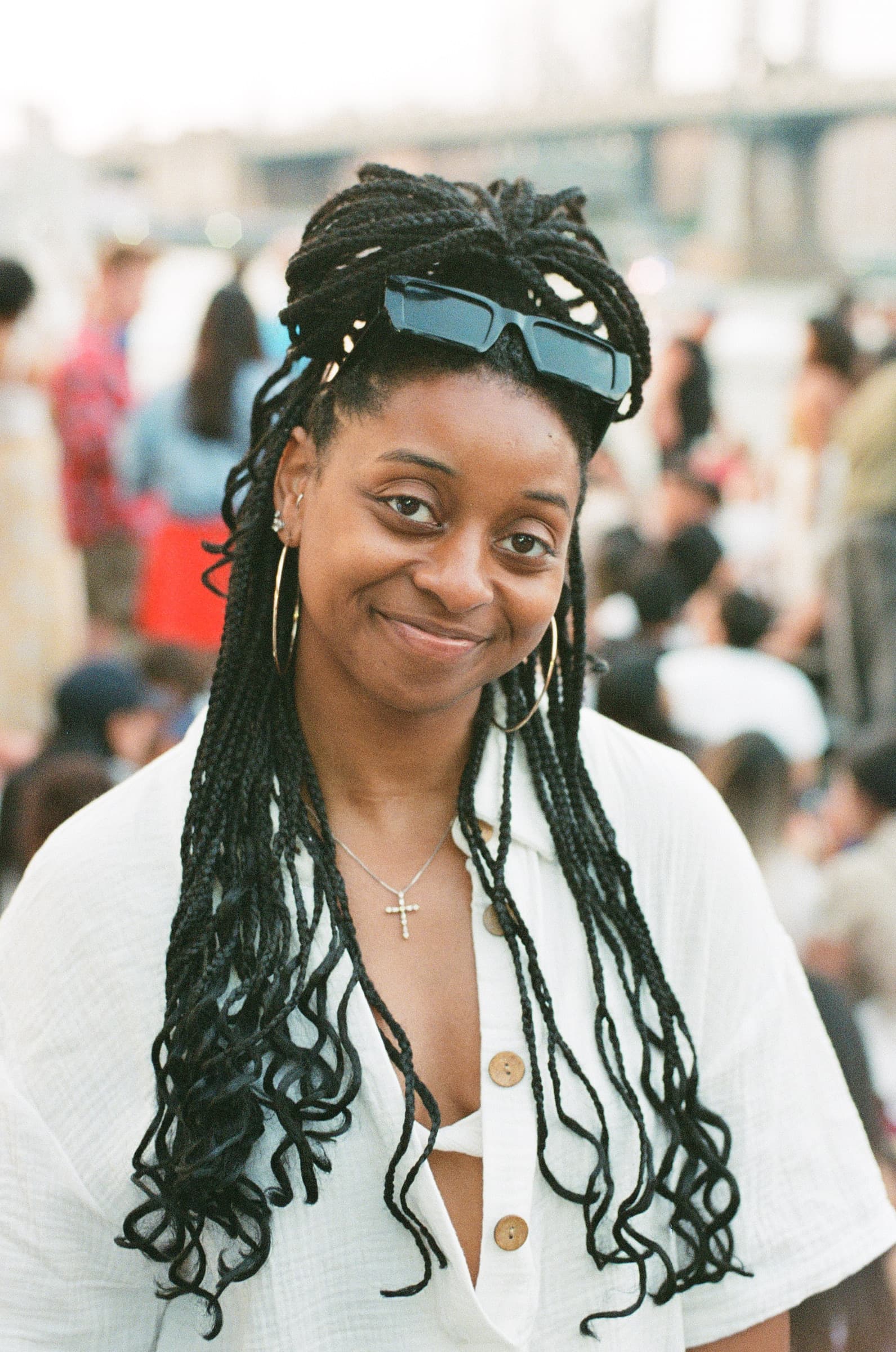 Portrait of a woman in a white shirt with glasses on her head, standing outdoors in front of a large gathering for a Fourth of July fireworks display