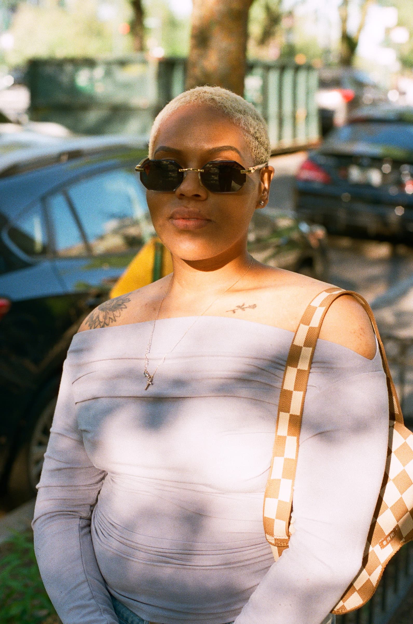 Portrait of a woman in a blue top holding a checkered clutch, wearing shades and staring into the camera